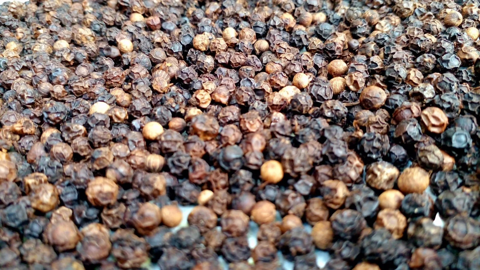 Black peppercorns scattered on dark stone surface with a wooden spoon, moody dramatic lighting, close-up macro shot