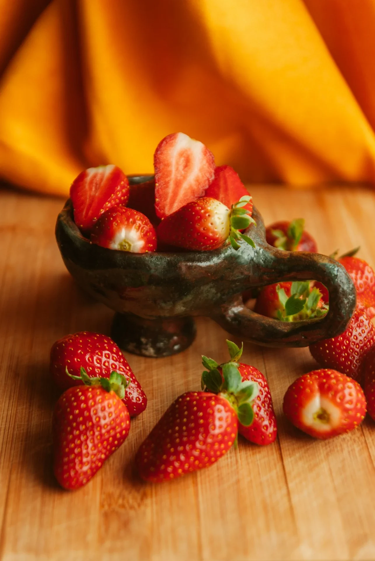 Fresh red strawberries in a dark ceramic bowl on wooden surface, vibrant red color against dark background, natural morning light